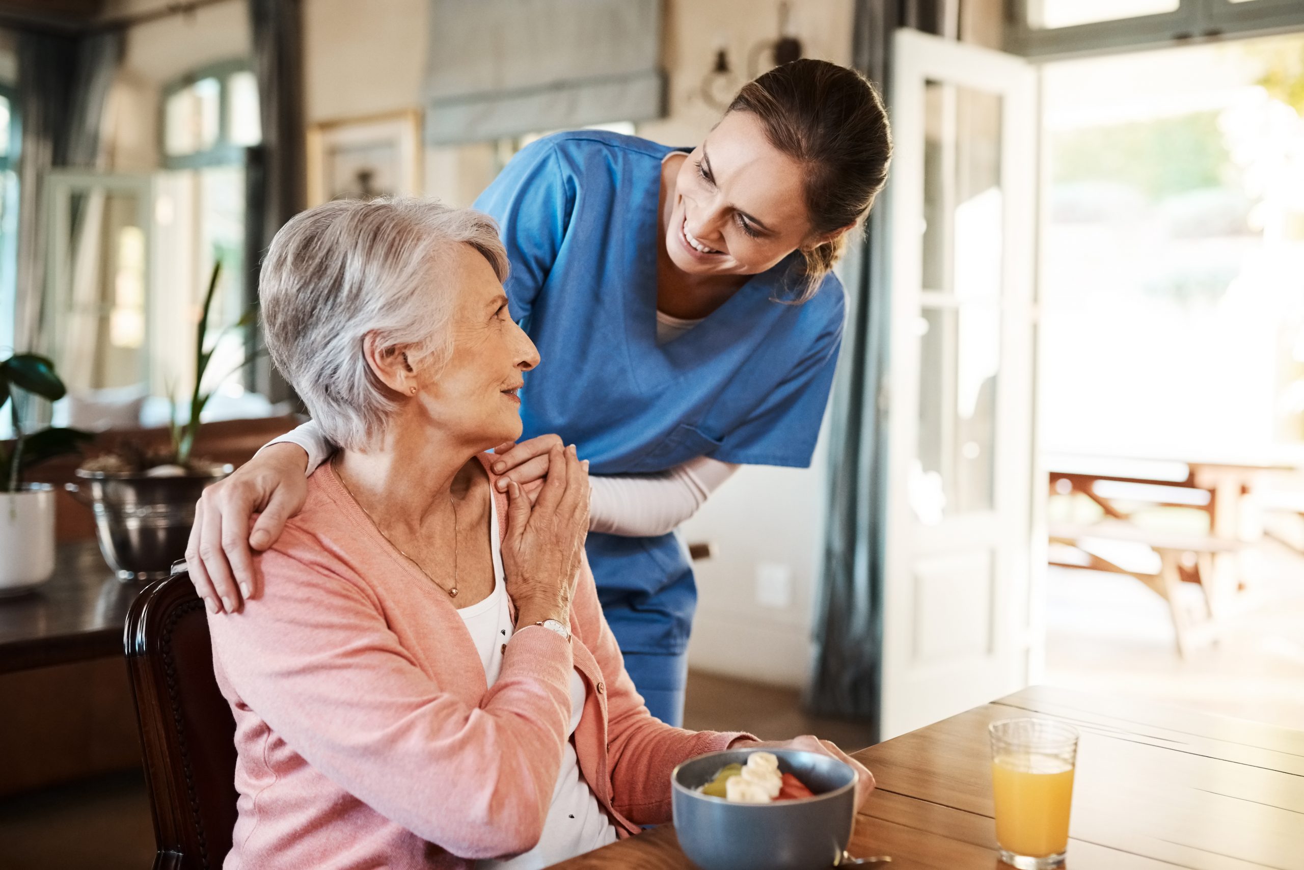 Are you enjoying your breakfast? Portrait of Smiling Senior Woman and Her Mixed Race Female Caregiver Together at Nursing Home. Caring Female Doctor Taking Care of a Happy, Elderly Woman